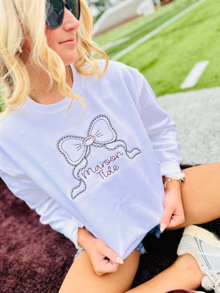 Person wearing a white sweatshirt with a bow design and 'Maroon 5' text, sitting outdoors.