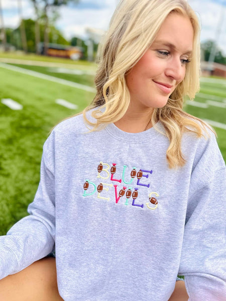 Person wearing a gray sweatshirt with 'Blue Devils' text and football icons on a sports field background