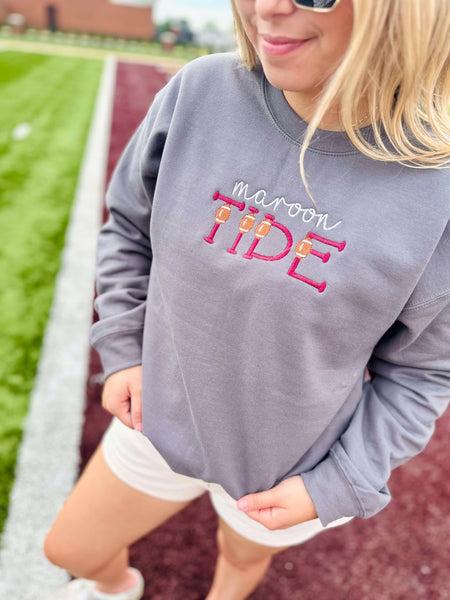 Person wearing a gray sweatshirt with 'maroon TIDE' text on a sports field background