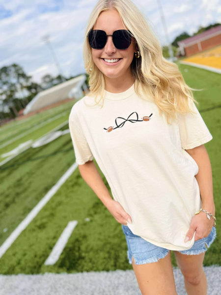 Woman wearing a cream t-shirt with a bow football design on a sports field