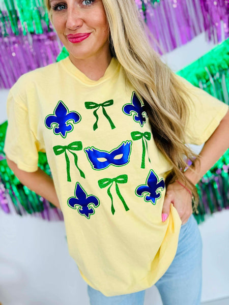 Woman wearing a yellow t-shirt with purple masks and green ribbons in front of a colorful background for Mardi Gras