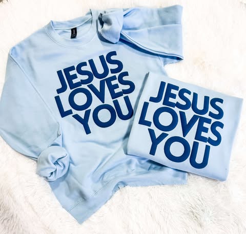 Two light blue sweatshirts with the text 'JESUS LOVES YOU' printed in blue puff vinyl on a white surface.