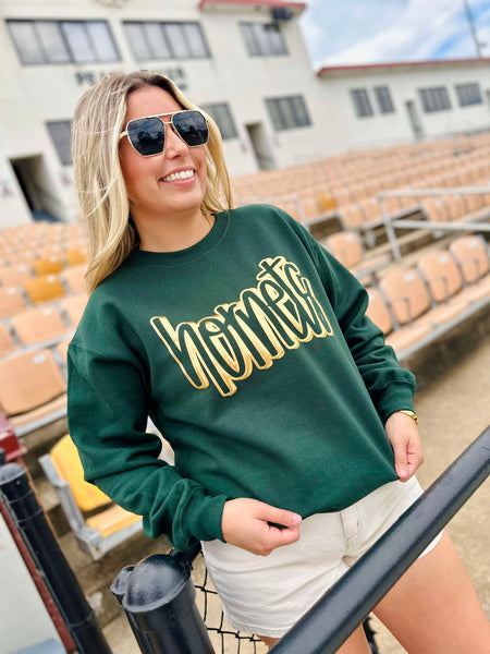 Woman wearing a green sweatshirt with 'Hornets' in gold letters, standing in an outdoor setting.