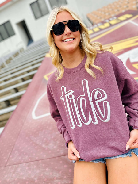 Woman wearing a purple sweatshirt with 'tide' text, standing outdoors.