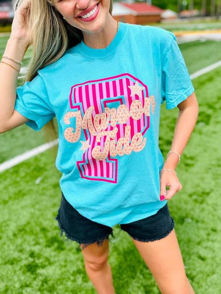 Woman wearing a blue t-shirt with a pink and white design on a grassy field