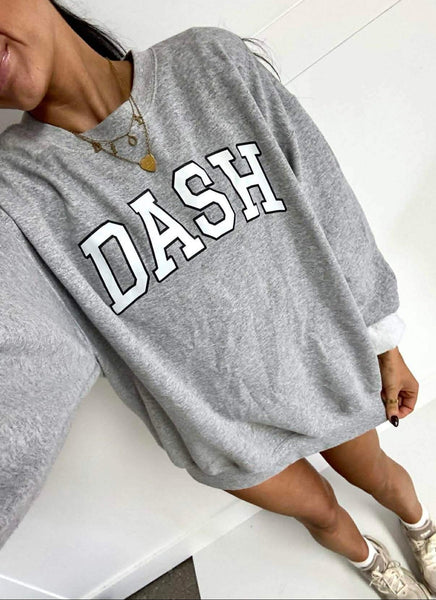 Person wearing a gray sweatshirt with 'DASH' printed on it, sitting on a white surface.