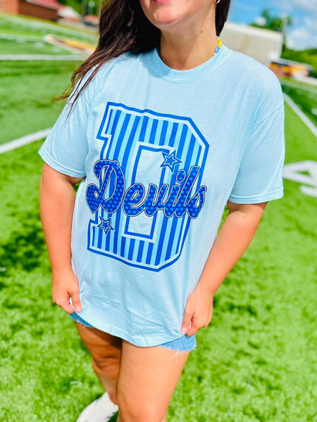 Person wearing a light blue t-shirt with 'Devils' printed on it, standing on a grassy field.