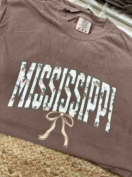 Brown t-shirt with 'Mississippi' printed on it, featuring a bow design, on a woven surface.