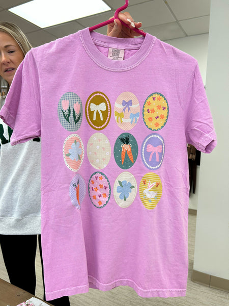 Purple t-shirt with colorful graphic designs on a hanger, held by a person.
