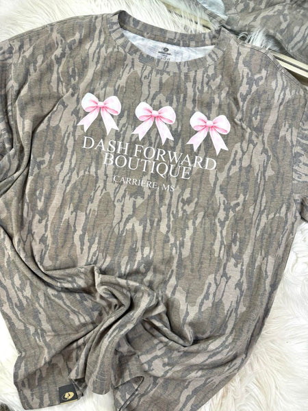 Mossy Oak Camouflage shirt with 'Dash Forward Boutique' text and pink bows on a white surface